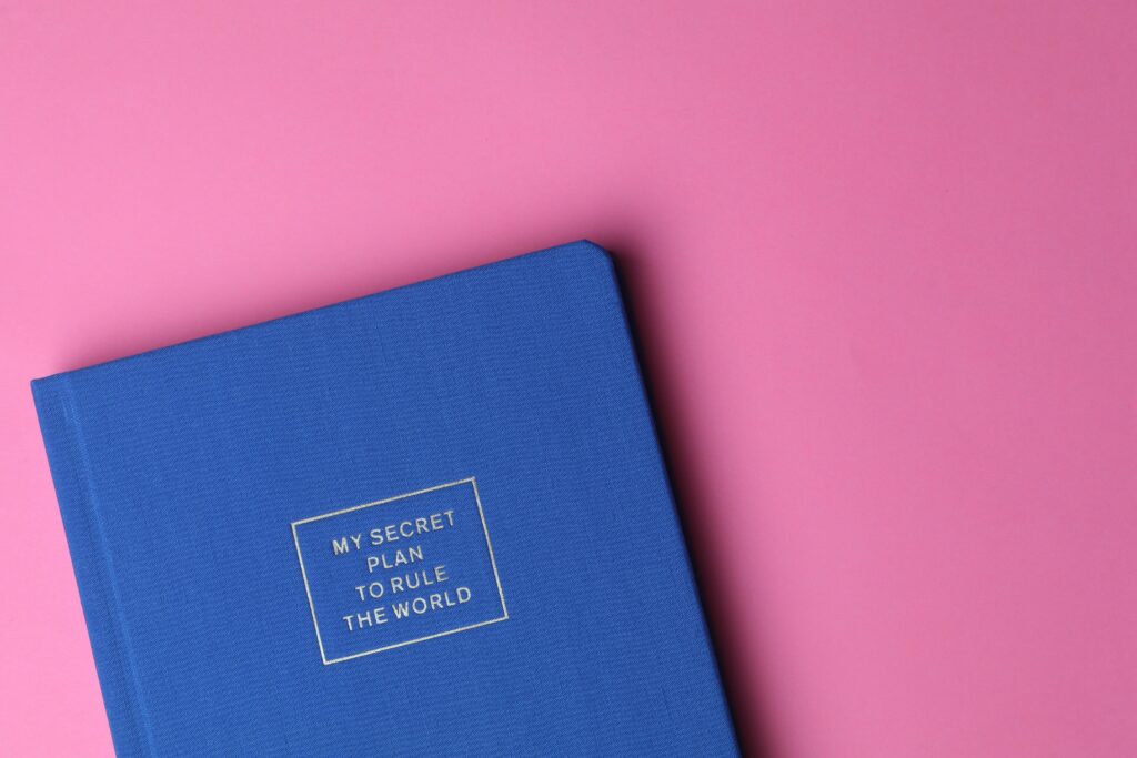 Stylish blue notebook on pink background with inspiring text cover.